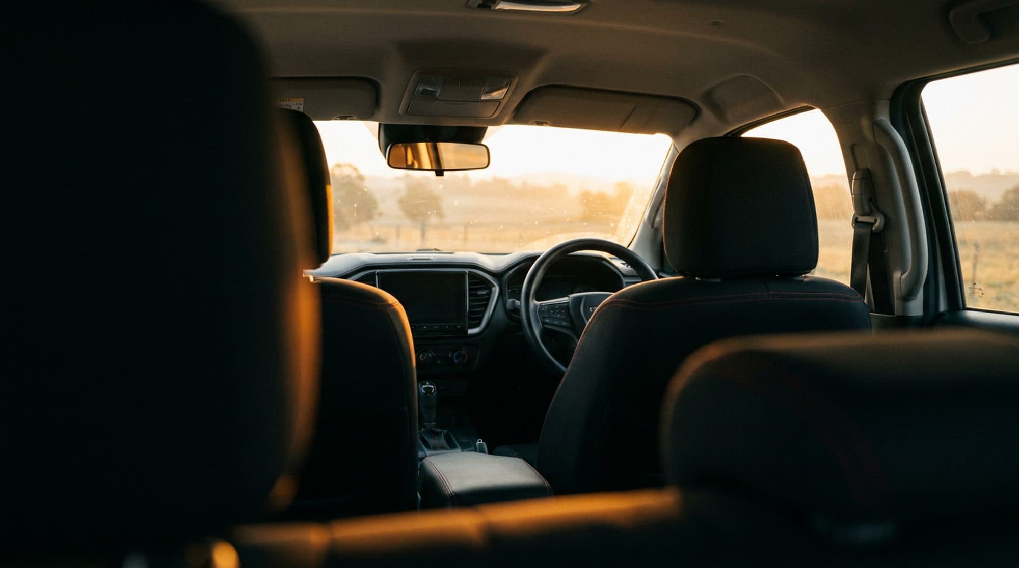 Front seats of a dual-cab ute fitted with black neoprene seat covers, lit by dawn light through the windscreen